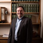 Professor Willie Wilson standing in front of dark wood bookshelves.
