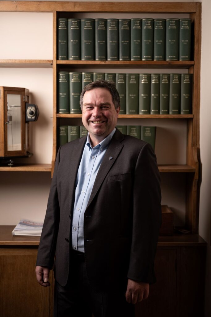 Professor Willie Wilson standing in front of dark wood bookshelves.