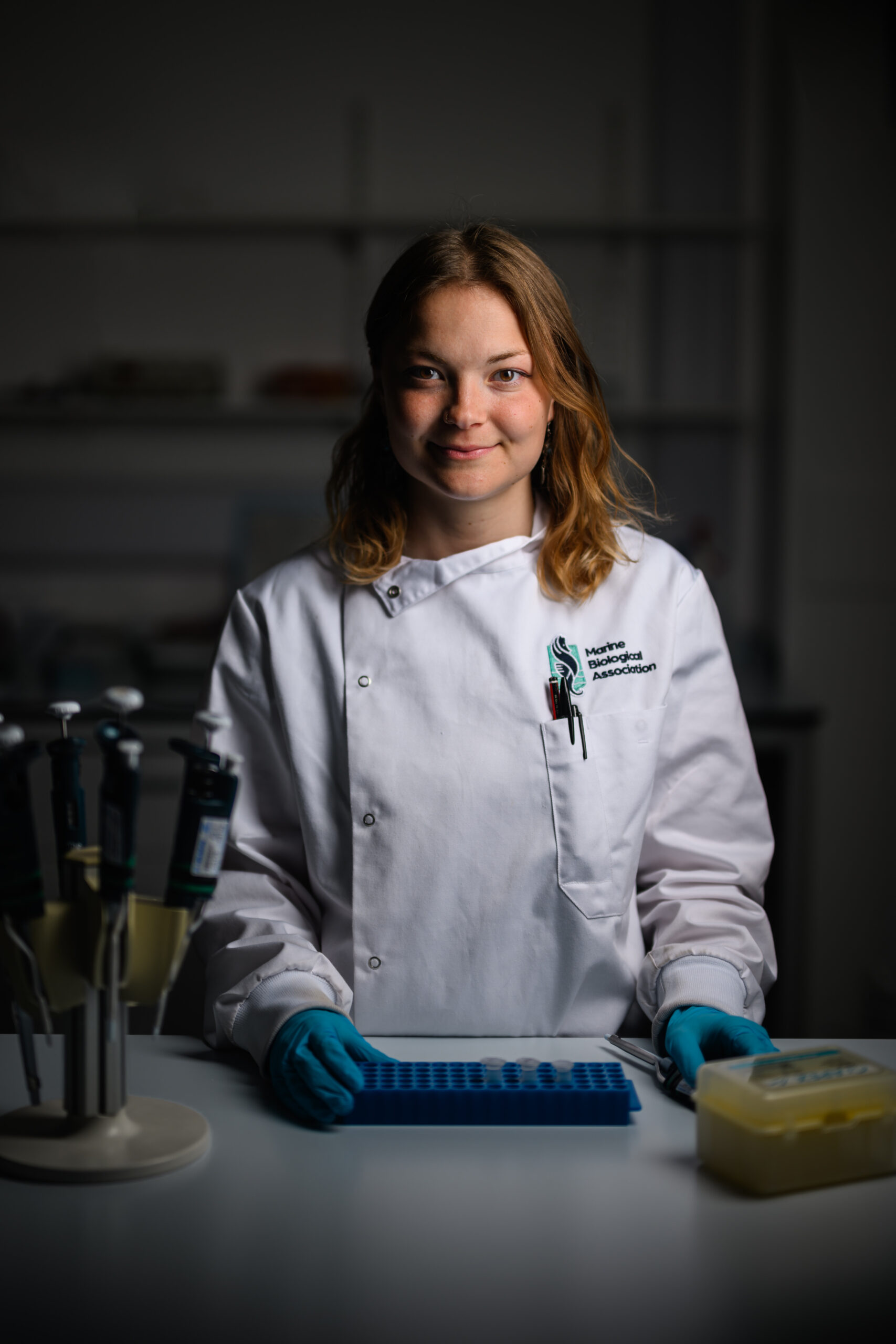 Rebekkah Uhl standing in lab coat with research equipment