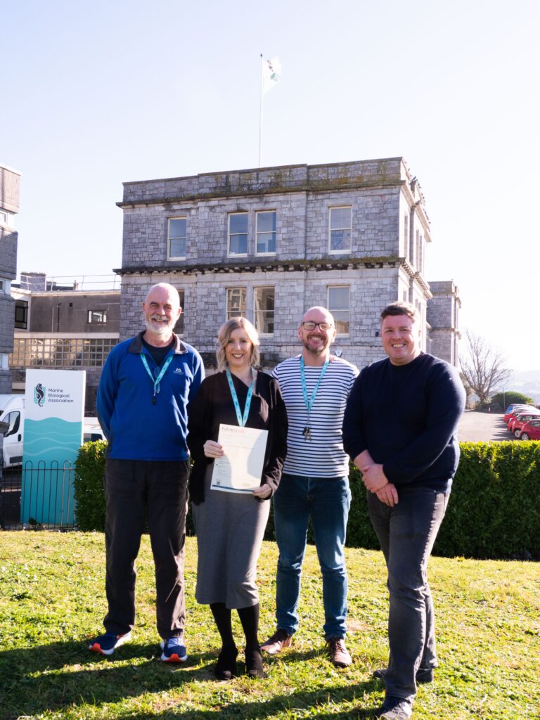 Supporting Mental Health in the Workplace: Mental Health staff smiling with certificate outside the MBA building on Citadel Hill.