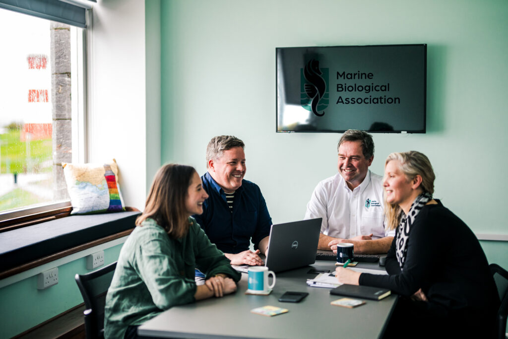 Group meeting with smiling SMT, Research Leads and Professor Willie Wilson in Drake's Island Meeting Room