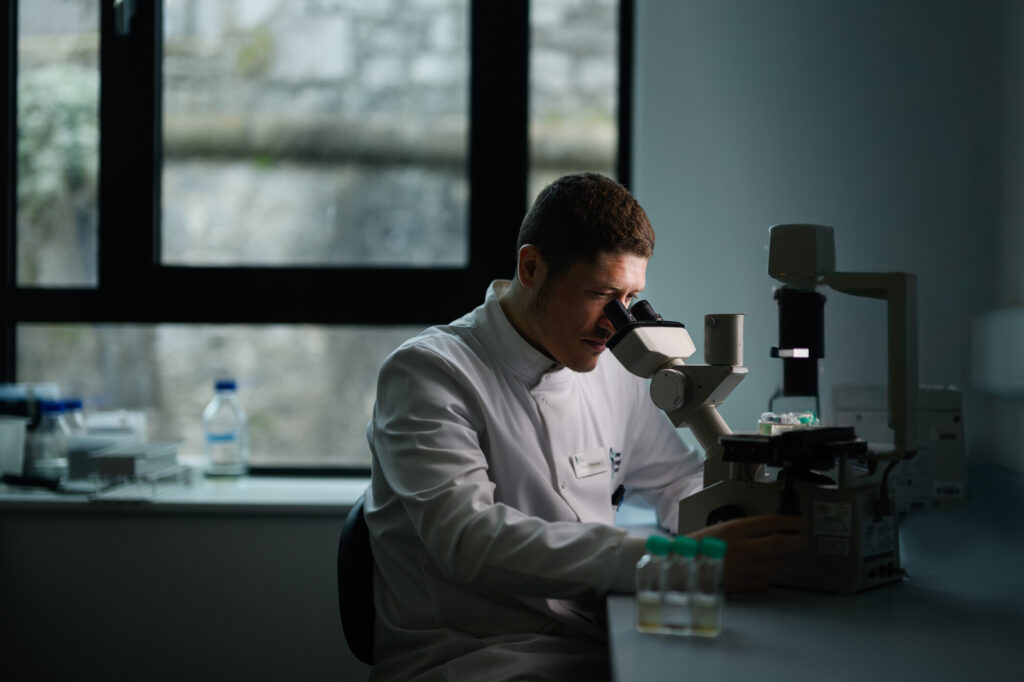 Hundred Diatom Genome Project man in lab coat looking at microscope MMCE