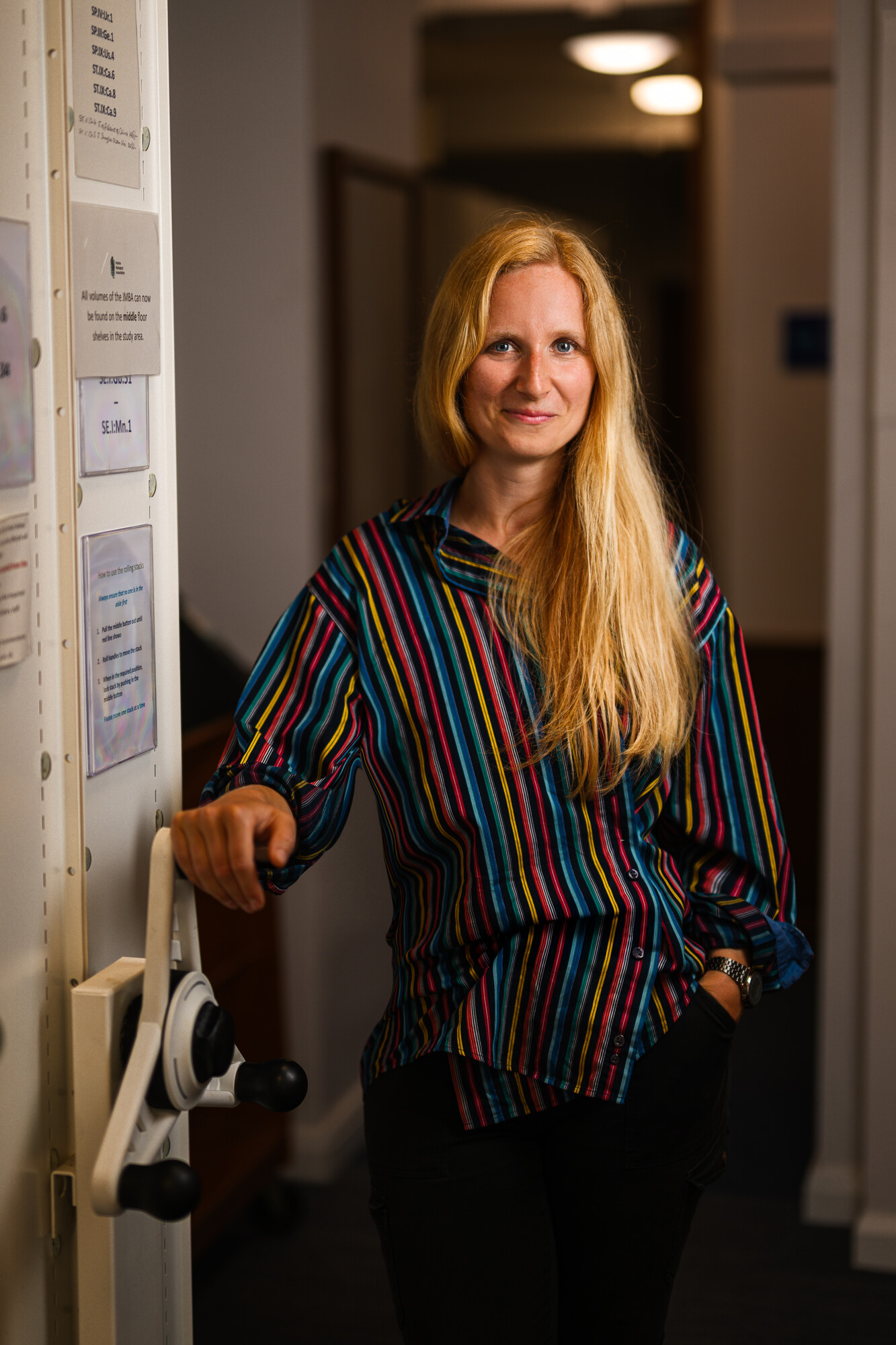 Emma Seal smiling, standing next to the MBA library of Journals