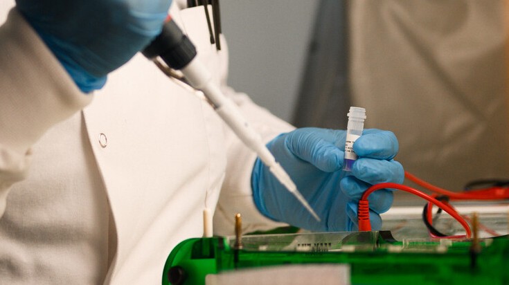 Close-up shot of a scientist's hands in blue gloves, holding a pipette and test tube.