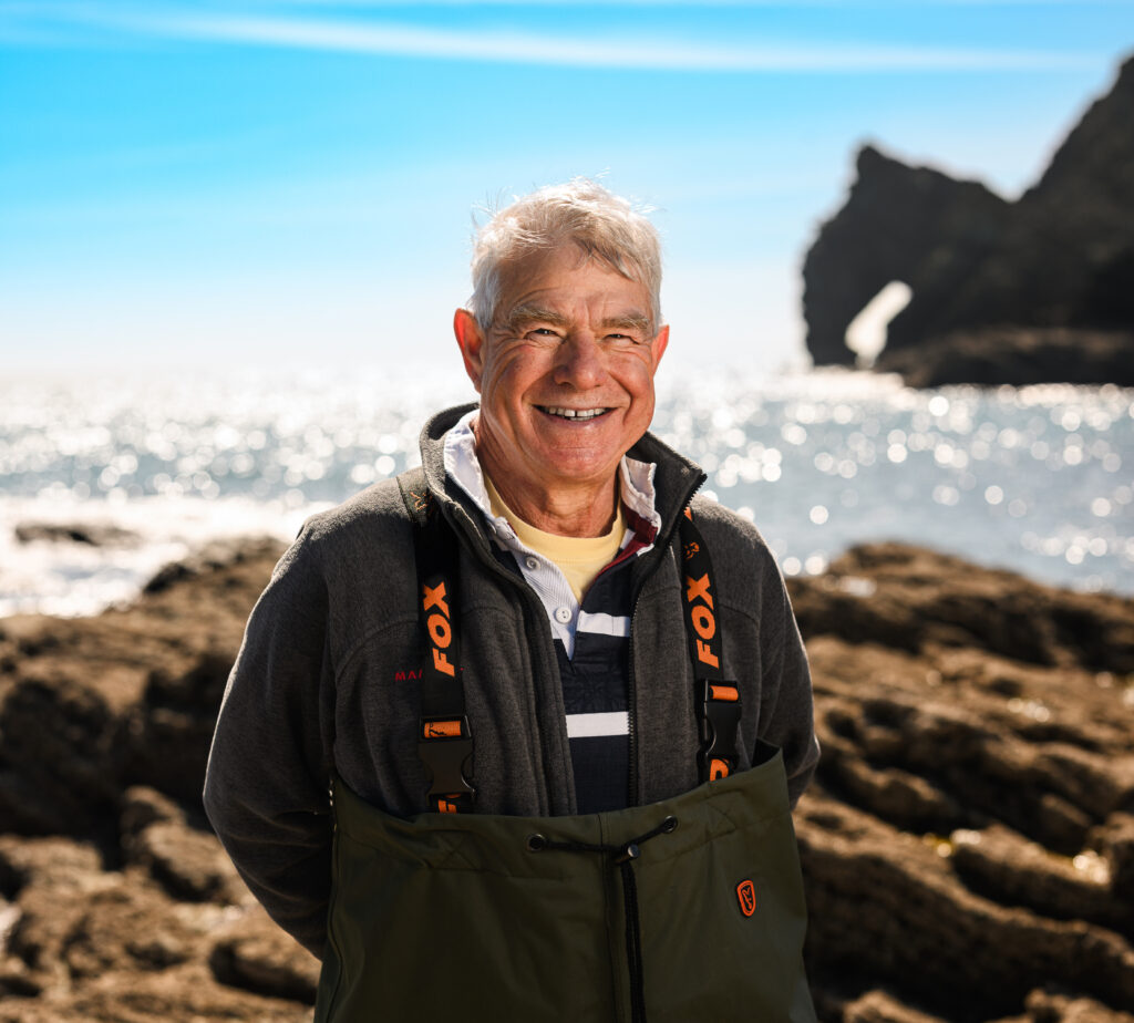Smiling scientist on a rocky shore.