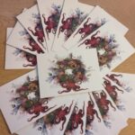 Cards featuring a Christmas 'Coral Wreath' illustration, fanned out in opposite directions with a card placed in the centre.