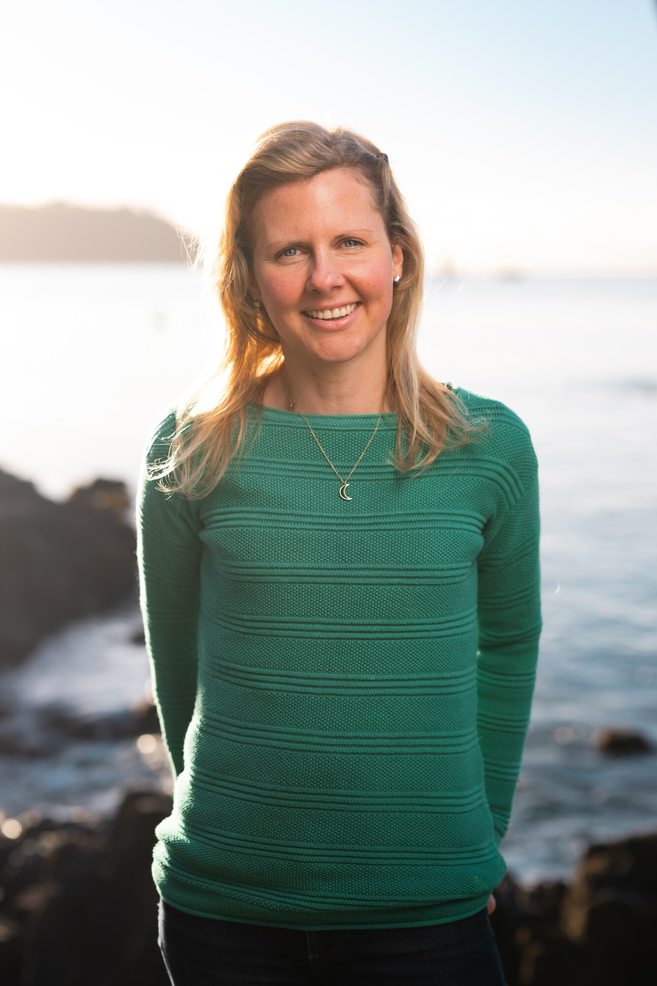 Dr Alice Horton, a young woman with long blonde hair and a green jumper, in front of a backdrop of sea and coastline.