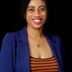Young woman of colour, wearing an orange and black crew neck jersey top under a cobalt blue smart casual jacket, smiles at the camera.
