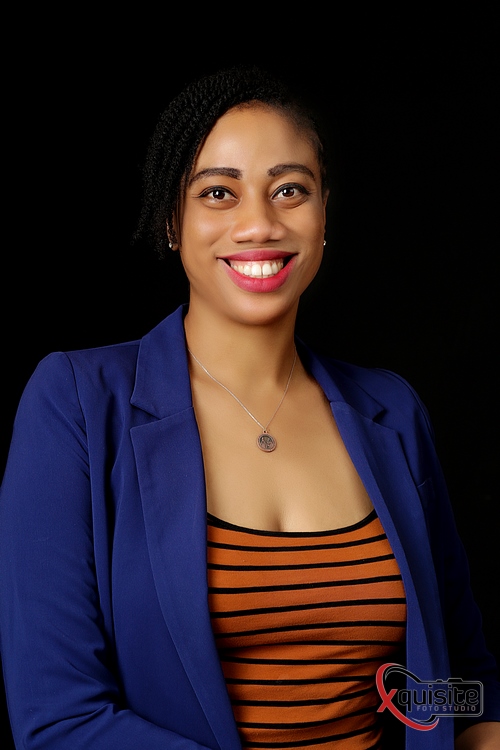 Young woman of colour, wearing an orange and black crew neck jersey top under a cobalt blue smart casual jacket, smiles at the camera.