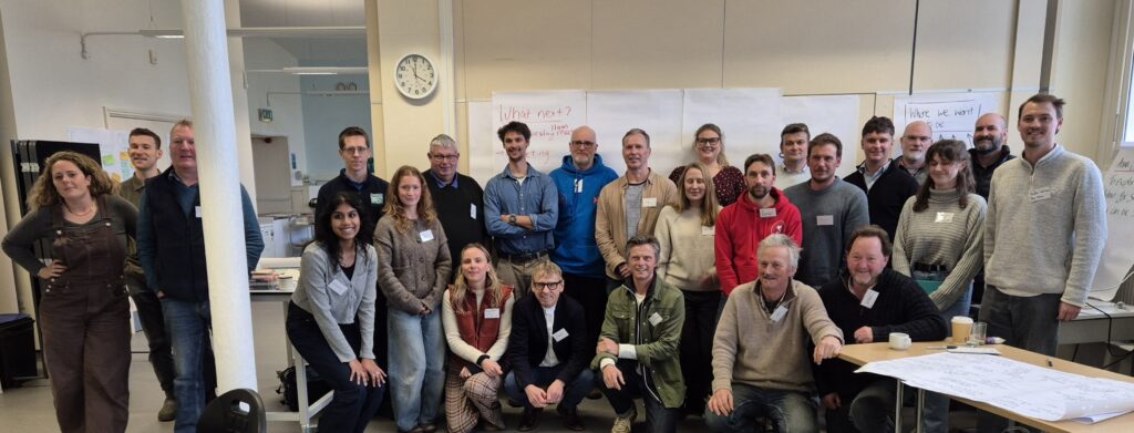 Group photo of adults of different ages in a large room with a clock in the background.