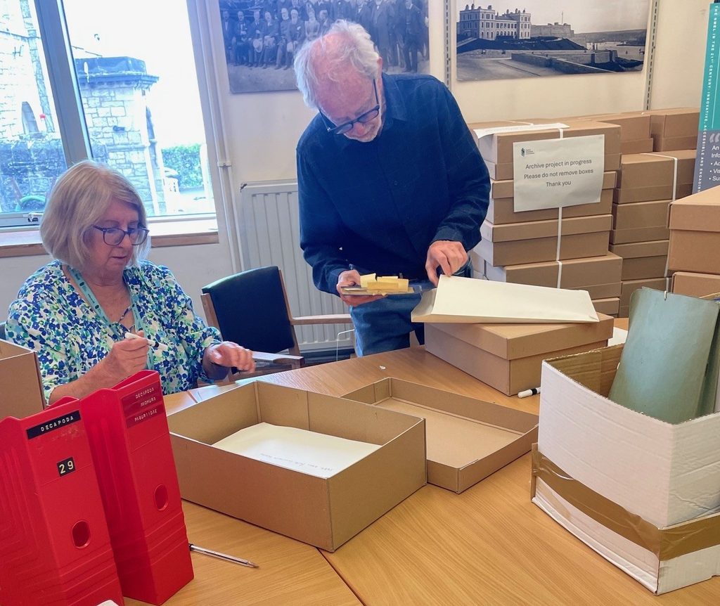 Bernie and Kathy putting objects and papers int boxes on a desk in the Library.